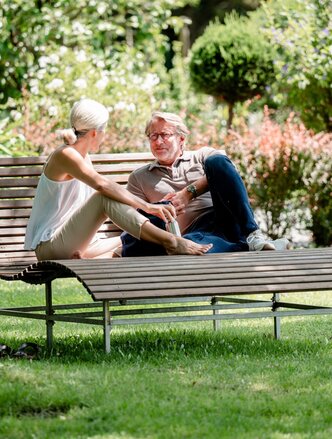 Zwei Personen auf einer Parkbank unterhalten sich während ihres Sommerurlaubs in Bad Füssing.